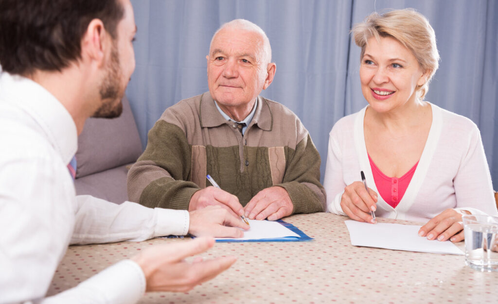 An elderly couple sitting with a financial advisor, discussing and signing documents.