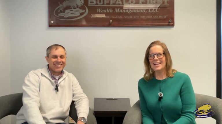 Two people smiling while sitting in front of a wealth management sign.